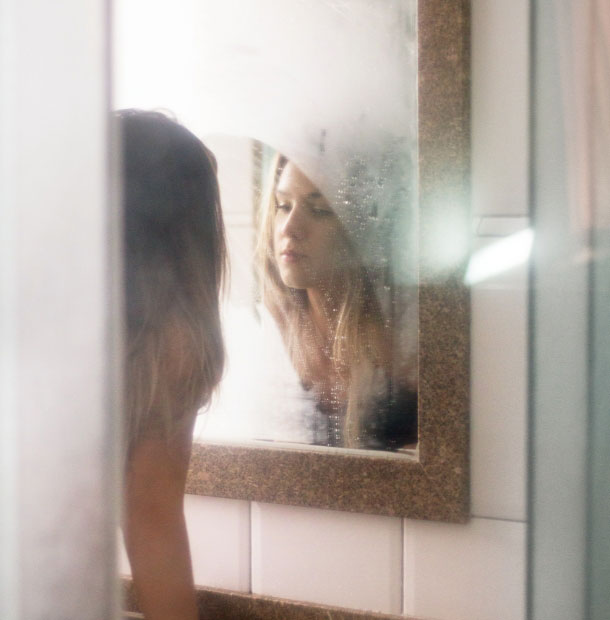 Frau schaut in einen beschlagenen Spiegel