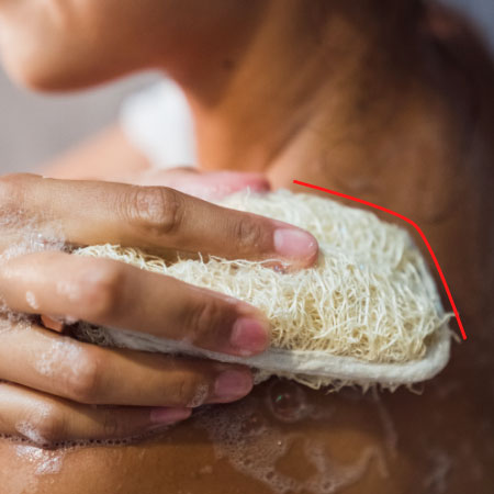 Detailaufnahme einer Frau in einer Dusche mit Luffaschwamm