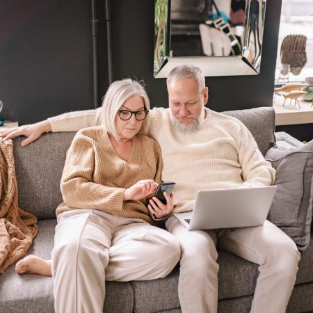 Älteres Paar schaut auf dem Sofa auf Handy und Laptop