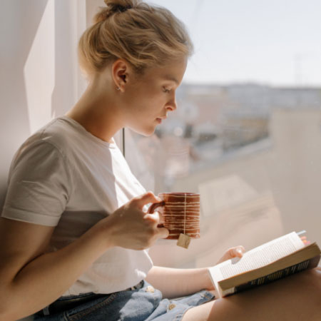 Junge Frau liest ein Buch vor einer Fensterfront